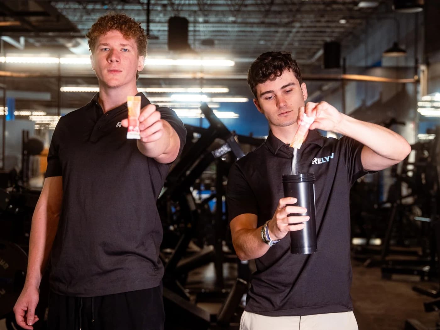 Relyv's two co-founders in the gym, one holding out a Relyv stick and the other pouring one into a shaker