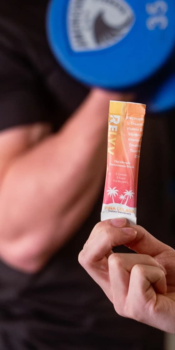 Hand holding a Relyv Performance Stack Piña Colada stick in front of an athlete mid-curl